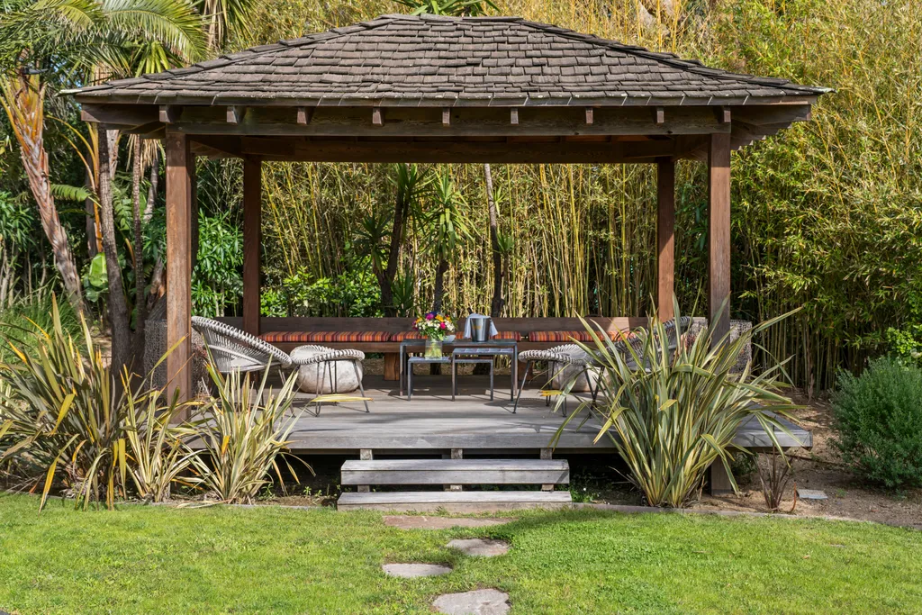 A timber garden pavilion with cushioned seating, backed by tall bamboo