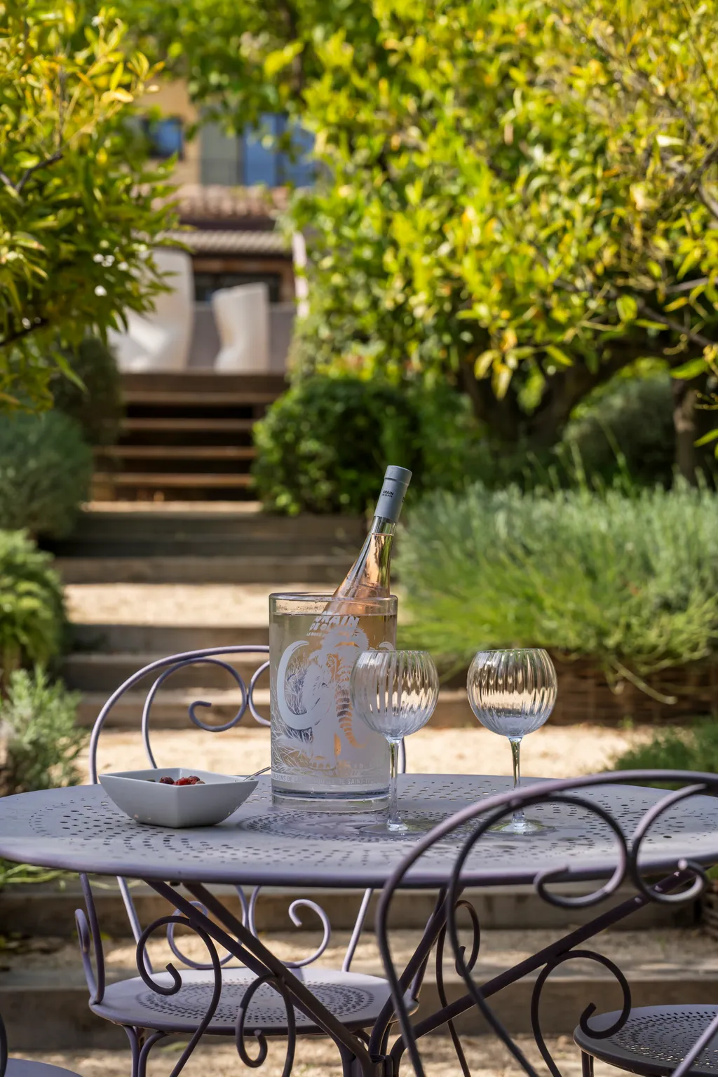 A garden table set with rosé, steps leading up to the villa between lemon trees