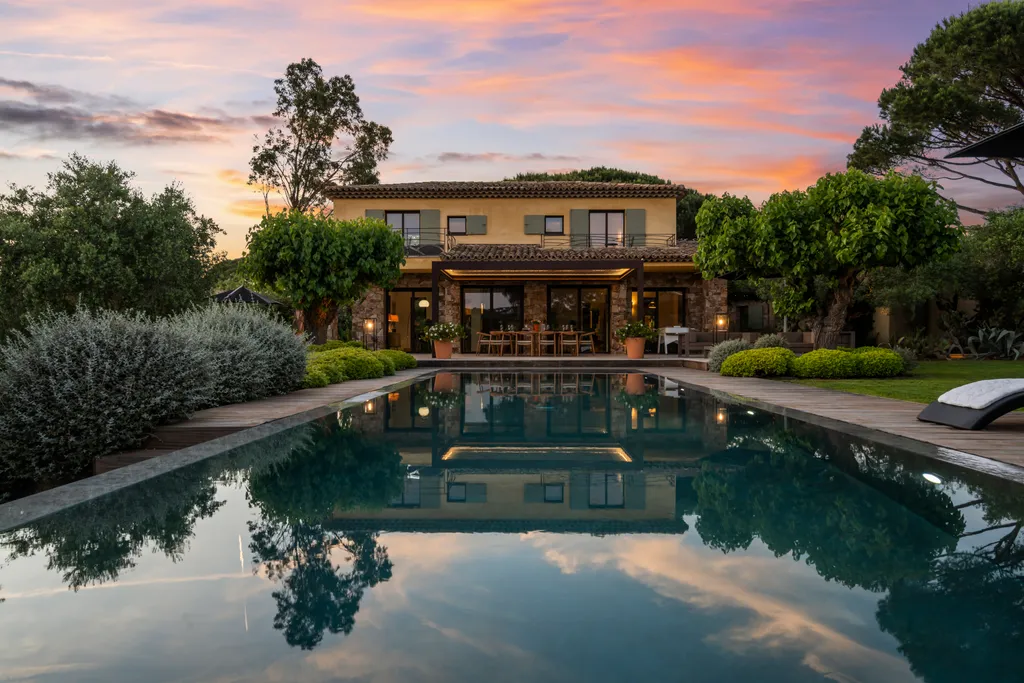 The villa's façade mirrored in the pool beneath a pink twilight sky