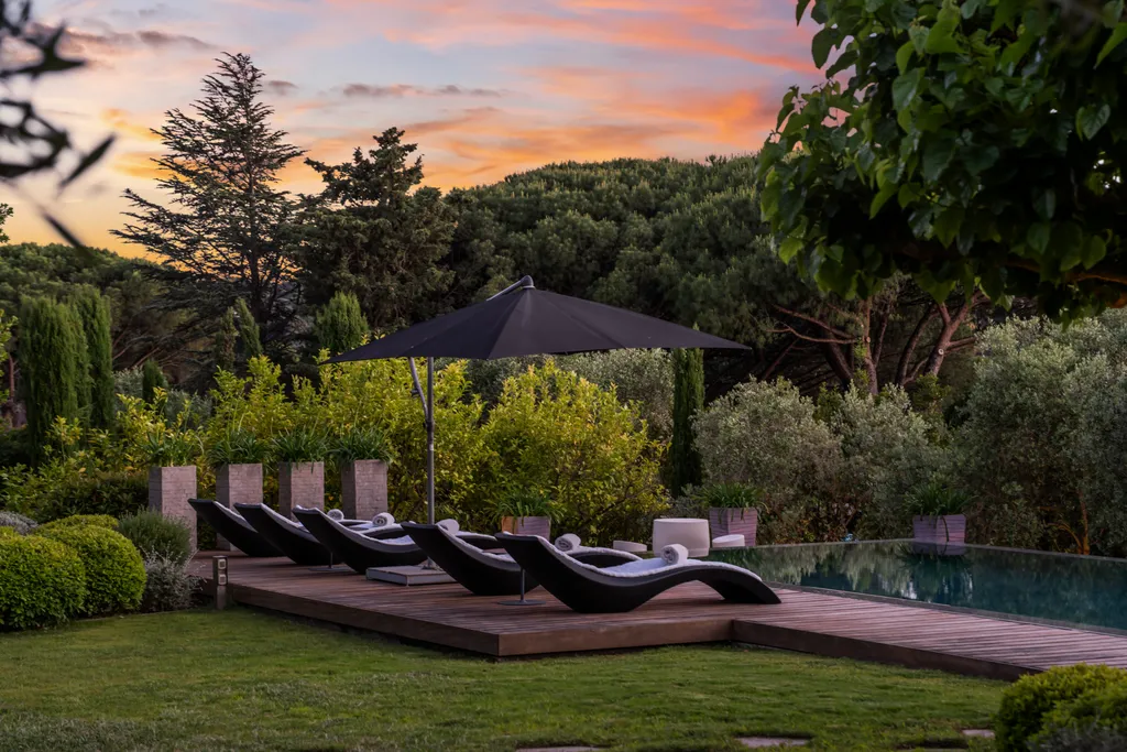 Black loungers on the pool deck beneath a parasol at sunset