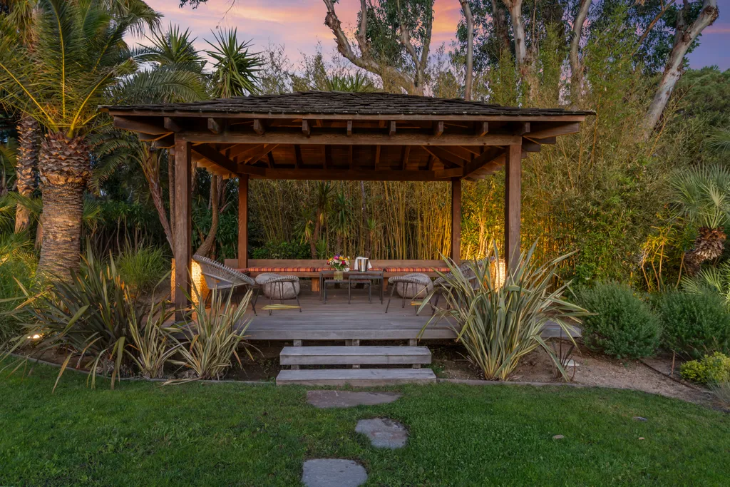 The lit garden pavilion at dusk, a palm rising beside it