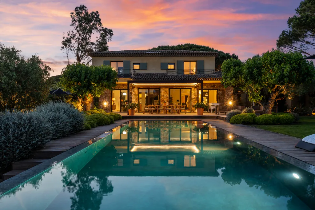 The illuminated villa mirrored symmetrically in the pool at twilight
