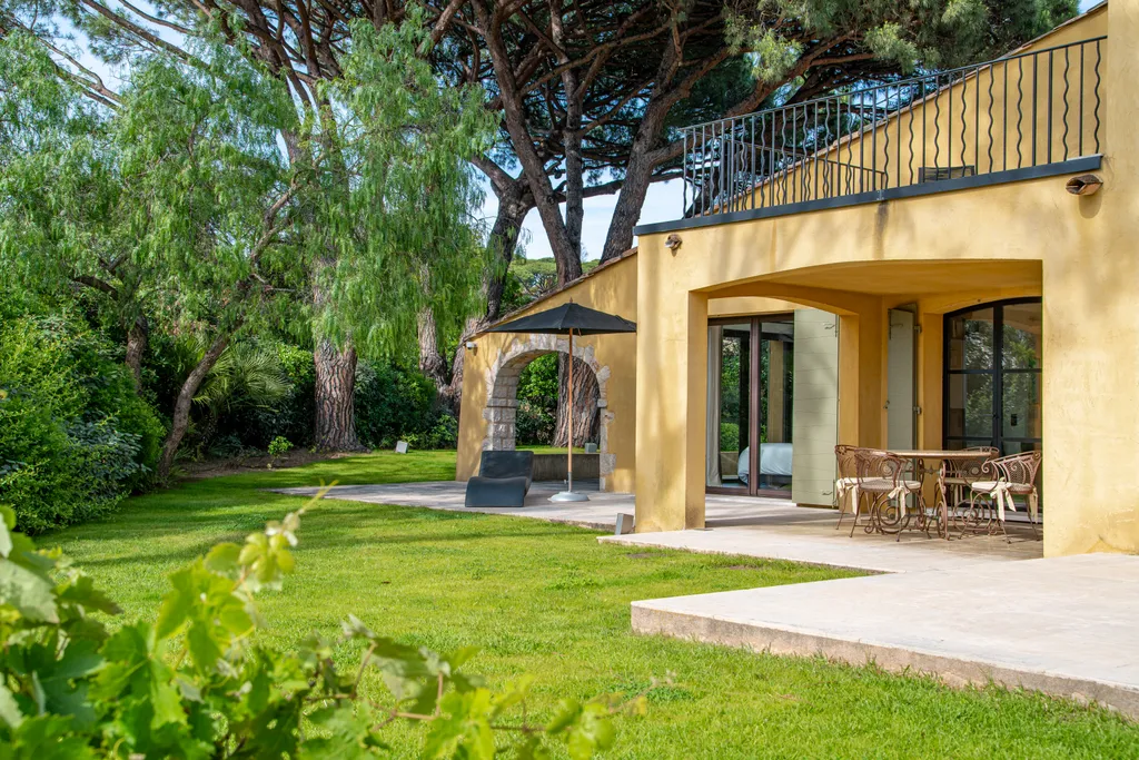 The villa's yellow façade and covered dining loggia seen from the garden