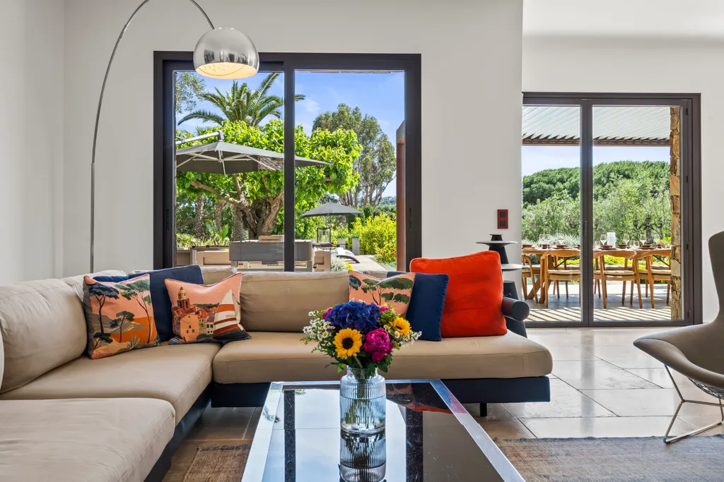 The villa's living room, its sofa facing terrace doors open to the garden and pool